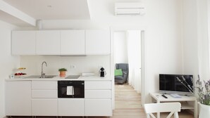 A modern kitchen with white cabinets, a built-in oven, and a sink. There is a dining area with a white table and chairs, and a TV on a stand. - THE RIVERSIDE SUITE and POOL near VENICE (Mira)