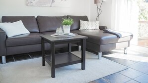 Un salon moderne avec un canapé marron foncé, une petite table basse agrémentée d’une plante et un tableau accroché au-dessus du canapé.