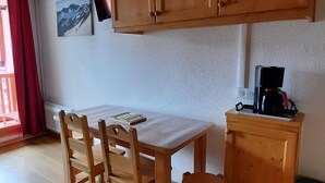 Een kamer met een houten eettafel, stoelen, een klein kastje en een wandtelevisie.