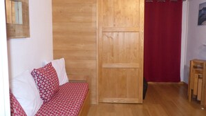 Een kamer met een houten garderobe, een rode gestreepte bank en een houten kruk.