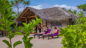 A beach hut with a thatched roof, surrounded by lush greenery.