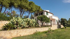 Un edificio de dos plantas con un muro de piedra y un jardín con cactus y árboles.
