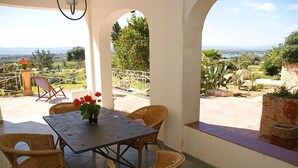 Un porche cubierto con muebles de mimbre y una mesa, con vistas a un paisaje pintoresco.