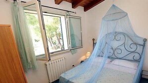 Un dormitorio con una cama con dosel, una ventana con cortinas, un radiador y una mesita de noche con lámpara.