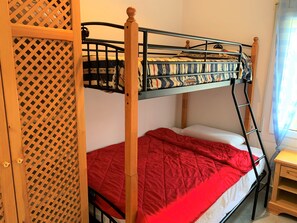 Una cama litera con un edredón rojo, una escalera de madera y una pequeña mesita de noche de madera.