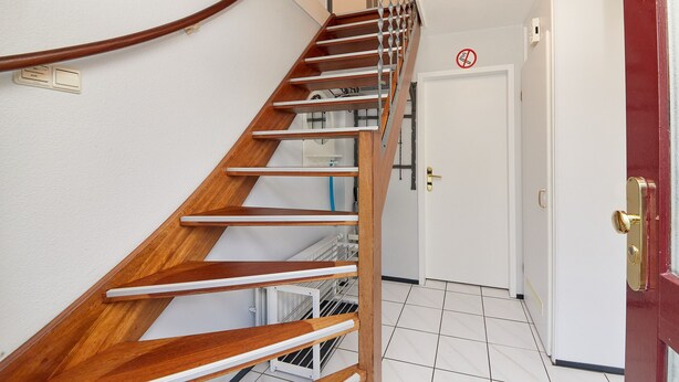 A wooden staircase with a metal handrail leading to a white door with a no-smoking sign. - Arrive & enjoy - Holiday home in Noordzeepark Ouddorp (Ouddorp)