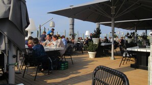 An outdoor dining area with tables and chairs, umbrellas, and potted plants.
