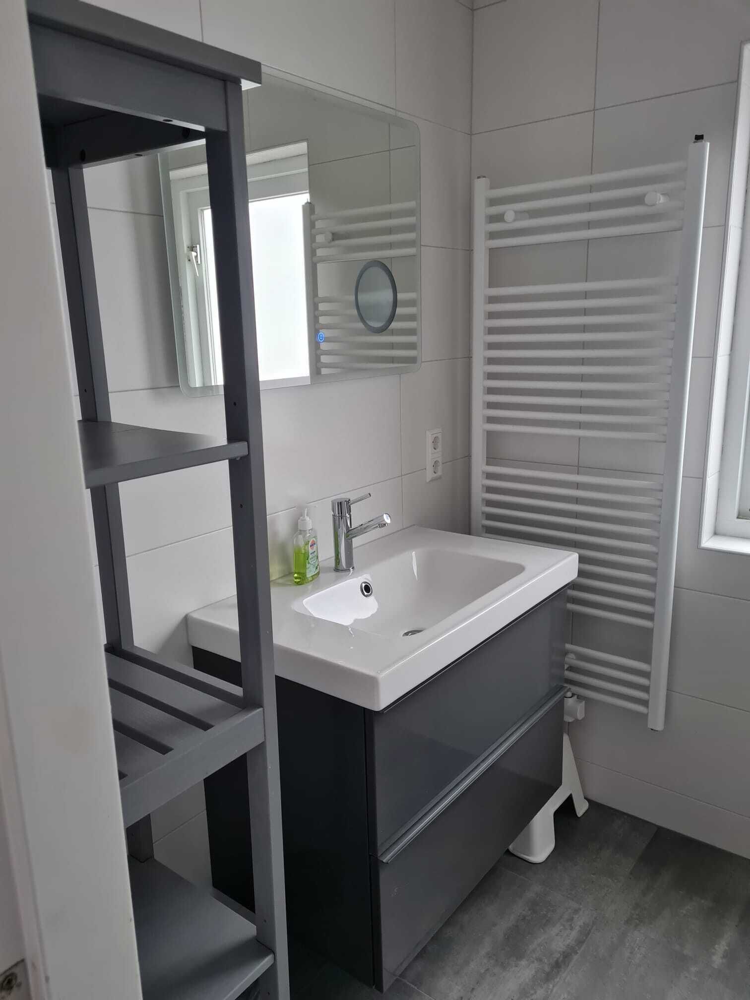 Uma casa de banho moderna com uma pia branca, um espelho, um porta-toalhas e um aquecedor embutido.
