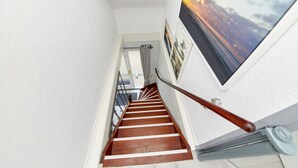 A staircase with wooden steps and a metal handrail, leading to a room with a view of the sky.