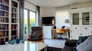 Een moderne woonkamer met een bank, salontafel, boekenkast, televisie, bureau met computer en een kast met glazen deuren.
