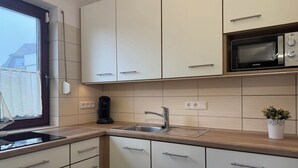 A modern kitchen with white cabinets, a stainless steel sink, and a microwave. - FeWo Seestern... at home on vacation (Büsumer Deichhausen)