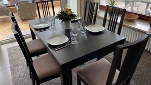 A dining area with a table set for six, chairs, a vase with flowers, and a view of the outdoors. - FeWo Seestern... at home on vacation (Büsumer Deichhausen)
