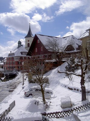 Une rue enneigée, avec une église, une grange rouge et un camion blanc garé dans la neige.