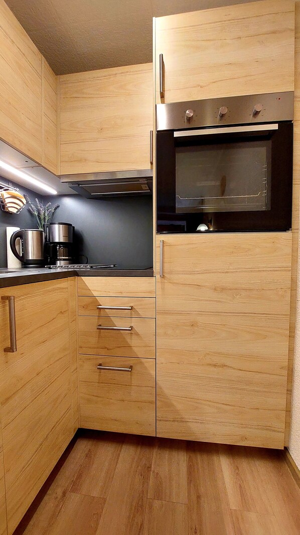 Een kleine keuken met houten kastjes, een inbouwoven en een koffiezetapparaat.