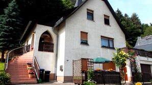 Una casa de dos pisos con un techo pronunciado, una chimenea visible y un pequeño porche con escalones que conducen a la entrada.