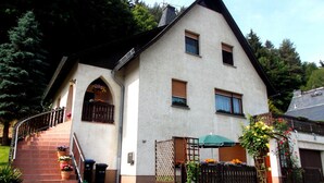 Una casa de dos pisos con un techo pronunciado, una chimenea visible y un pequeño porche con escalones que conducen a la entrada.