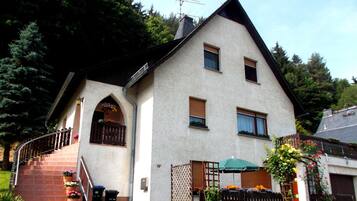 Ein zweistöckiges Haus mit einem steilen Satteldach, einem sichtbaren Schornstein und einer kleinen Veranda mit Stufen zum Eingang.