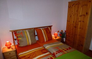 Un dormitorio con cama, almohadas, una mesita de noche, una lámpara y un armario de madera.