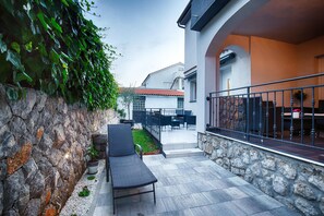 A patio with a stone wall, a black lounge chair, and a dining area with outdoor furniture. - KRK CITY !! 250m PROMENADE !!Vilaveja family house !!small pool, jacuzzi (KRK)