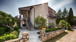 Ein zweistöckiges Haus mit Naturstein-Fassade, einem Balkon und einem kleinen Garten mit Steinmauer und Pflanzkübeln.
