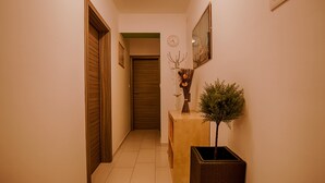 Ein Flur mit einer Holztür, einem geschlossenen Rolltor, einem Konsolentisch mit einer Vase und einem kleinen Baum sowie einer Uhr an der Wand.