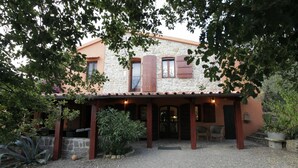Ein Steinhaus mit überdachter Terrasse, umgeben von Bäumen und Pflanzen.