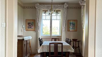 Comedor con mesa dispuesta para cuatro, una araña y una ventana con cortinas.