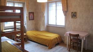 Una stanza con un letto a castello, un letto singolo, una scrivania con una sedia e una lampada a sospensione.