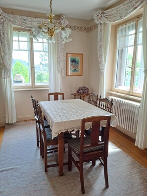 Una sala da pranzo con un tavolo apparecchiato per quattro persone, circondato da sedie, un lampadario e tende floreali.