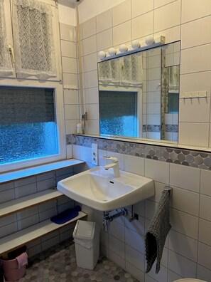 Un bagno con un lavandino bianco, uno specchio sopra, una finestra con vista e un pavimento piastrellato.