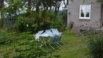 Un jardín con una mesa y sillas de metal, rodeado de follaje y plantas con flores.