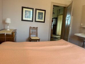 Una camera da letto con un letto, una sedia, una cassettiera, una lampada e due quadri appesi al muro.