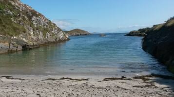 A coastal beach with rocky cliffs and calm waters.
