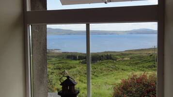 A window with a view of a coastal landscape, a lighthouse model, and a seashell.