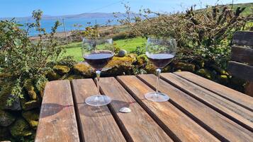 Two wine glasses on a wooden table with a view of the sea and hills in the background.