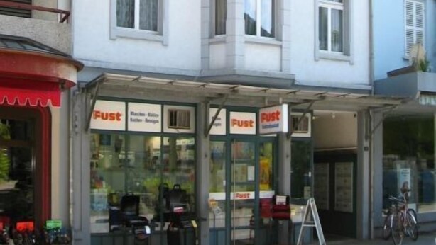 Un immeuble à plusieurs étages dont le rez-de-chaussée abrite un magasin dont l’enseigne est « Fust ».