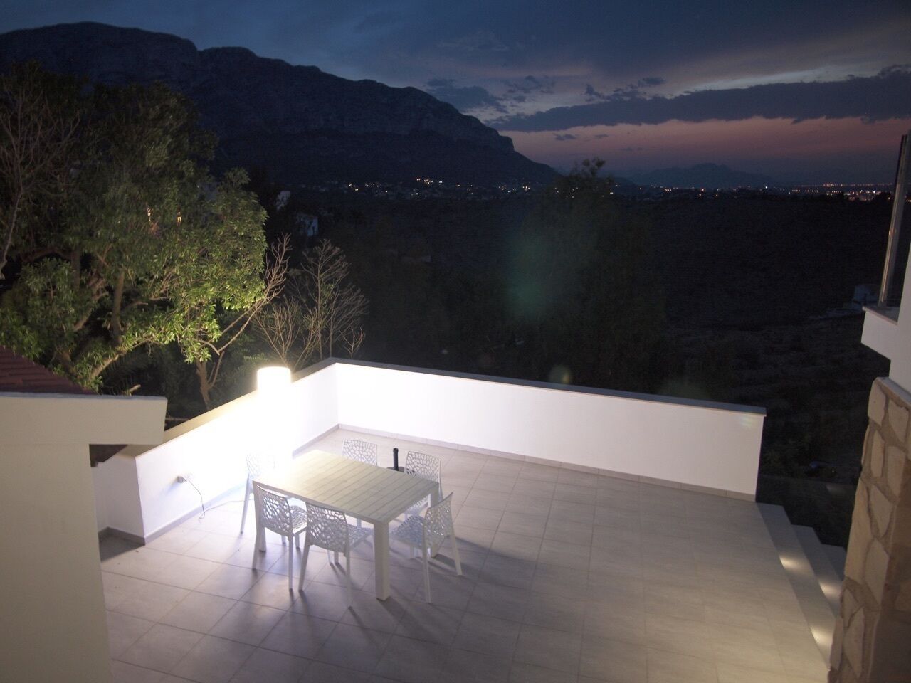 An outdoor patio with a table and chairs, overlooking a mountainous landscape at dusk.