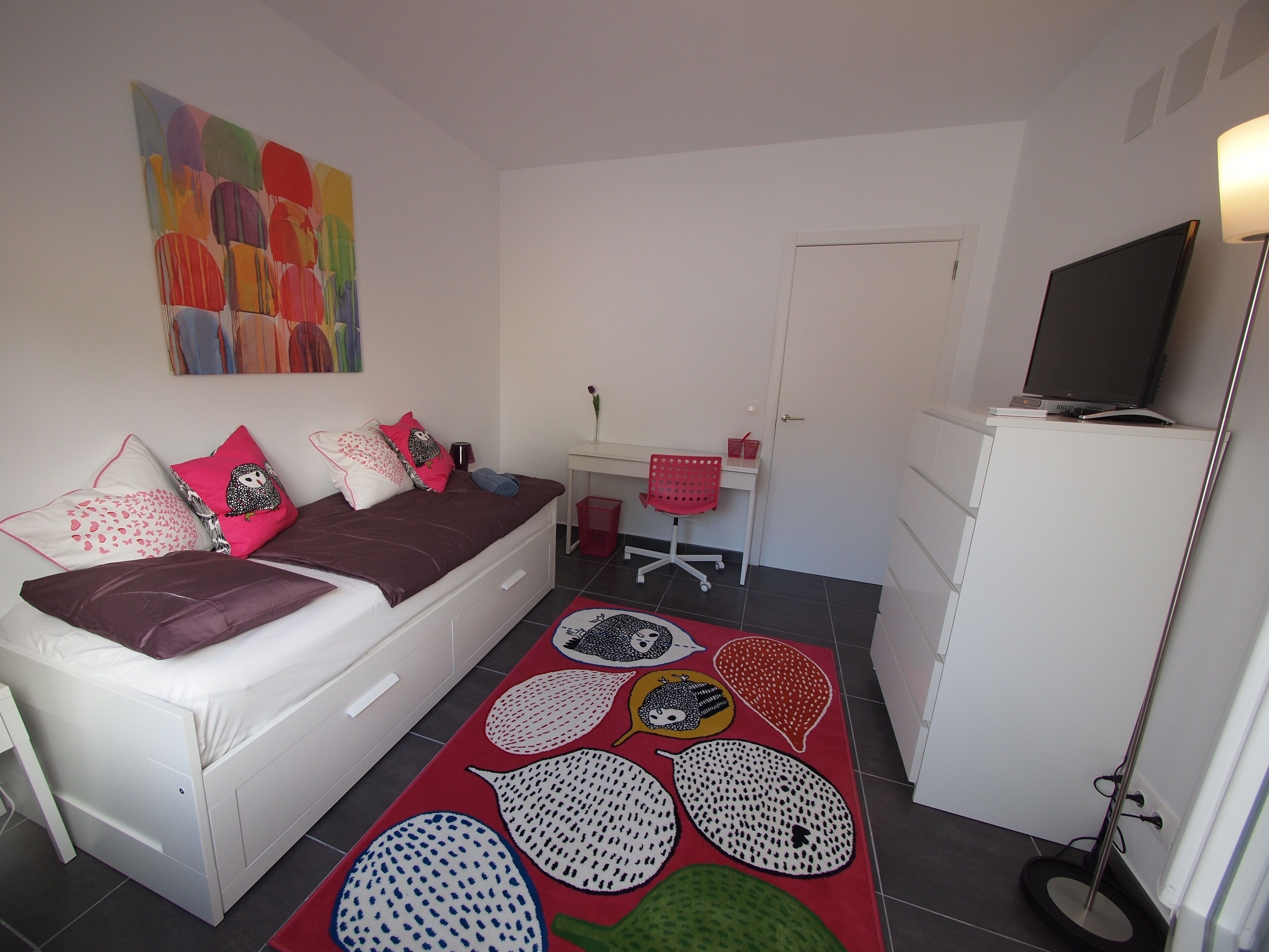 A bedroom with a bed, desk, chair, and a television.