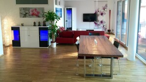 A modern living room with a wooden dining table, red sofa, and a potted plant.