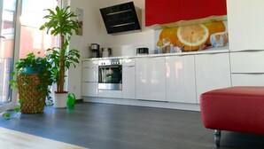 A modern kitchen with white cabinets, a red accent wall, and a large window.