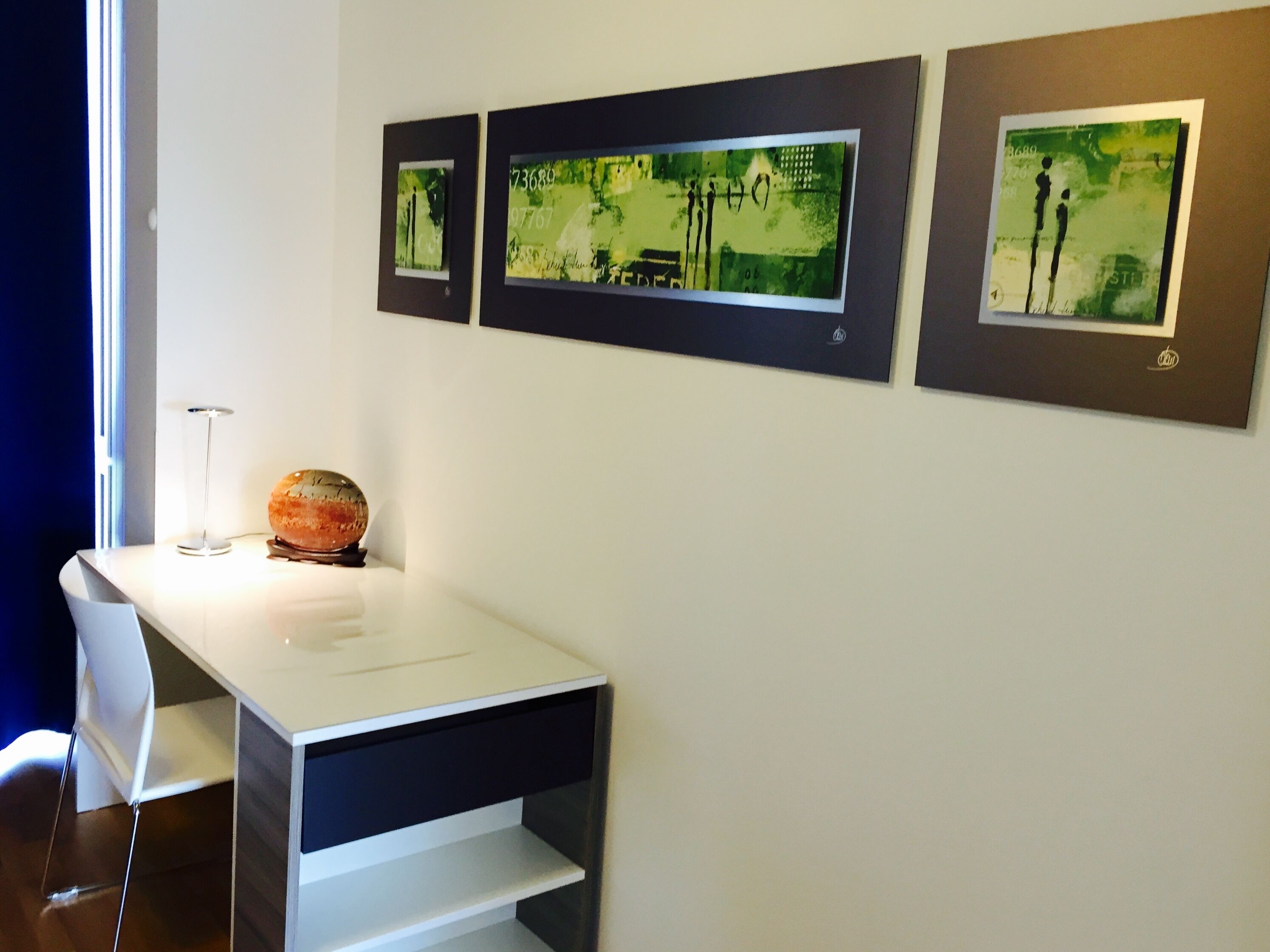 Une pièce moderne avec une table blanche, deux chaises et trois œuvres d’art encadrées accrochées au mur.