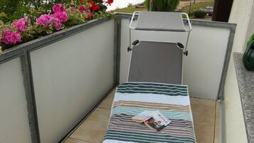 Un petit balcon avec un seul fauteuil, une vue sur un lac et un jardin parsemé de fleurs roses.