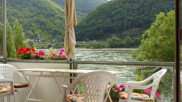 A balcony with a table and chairs, overlooking a river and forested hills.