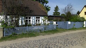 A cobblestone street leading to a white building with blue shutters and a tiled roof. - Uckermark old farmhouse with large wild garden (Templin)