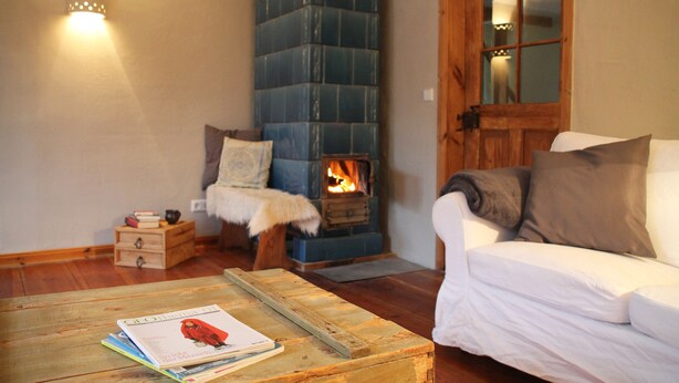 A cozy living room with a wood-burning stove, a white sofa, and a wooden coffee table with books. - Uckermark old farmhouse with large wild garden (Templin)