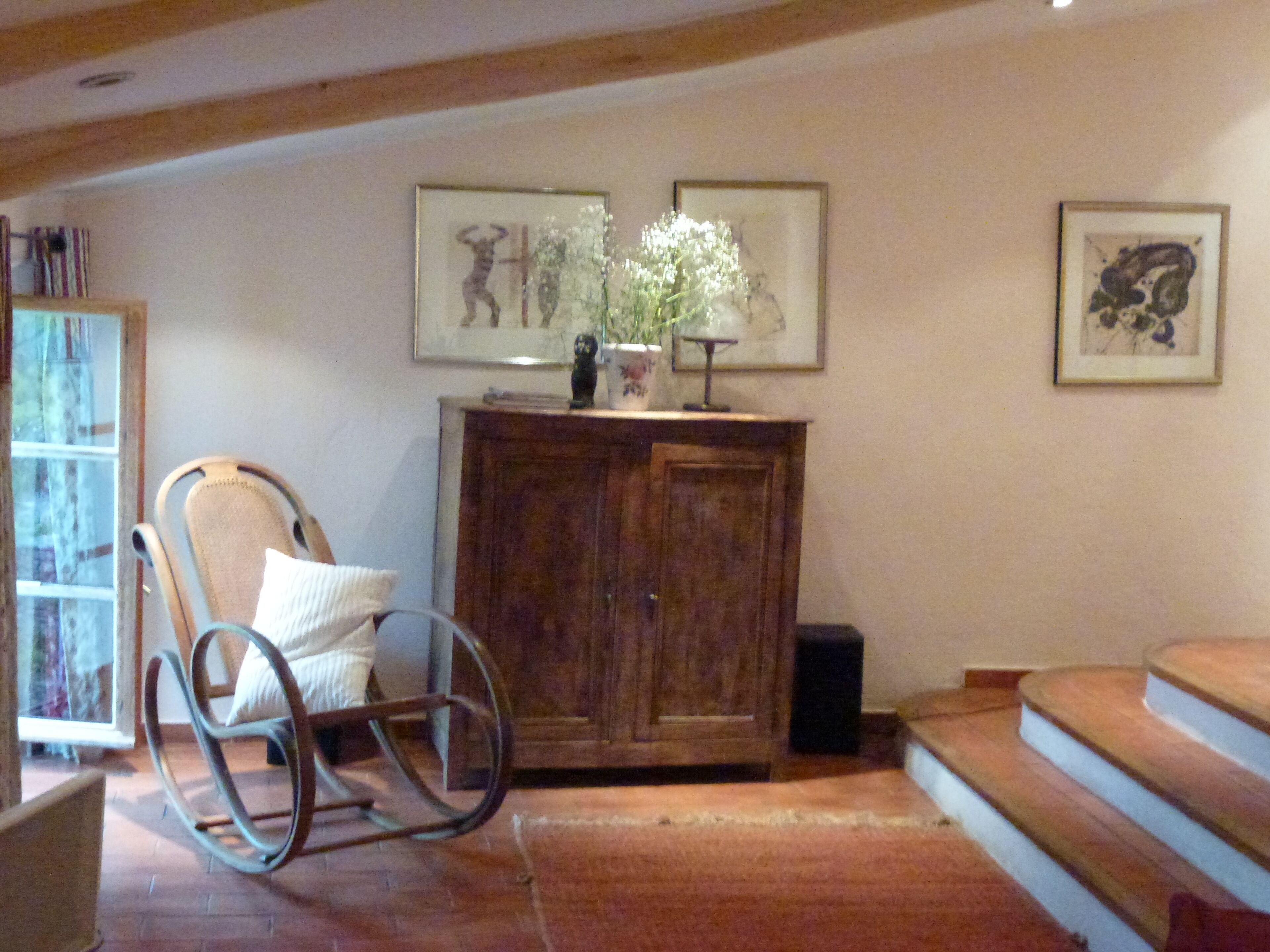 A living room with a rocking chair, a wooden cabinet, and a staircase.