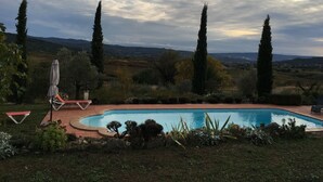 Piscina rodeada de un jardín con cipreses y vistas a colinas distantes.