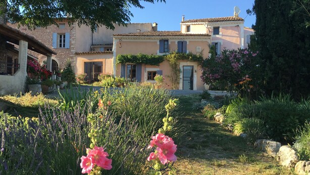 Una villa de estilo mediterráneo tradicional, con jardín, muros de piedra y un cielo azul despejado.