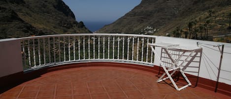 Una terraza con barandilla blanca curva, una silla plegable blanca y vistas a un paisaje montañoso.