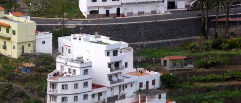A coastal residential area with white buildings, some with balconies, and a road with vehicles.
